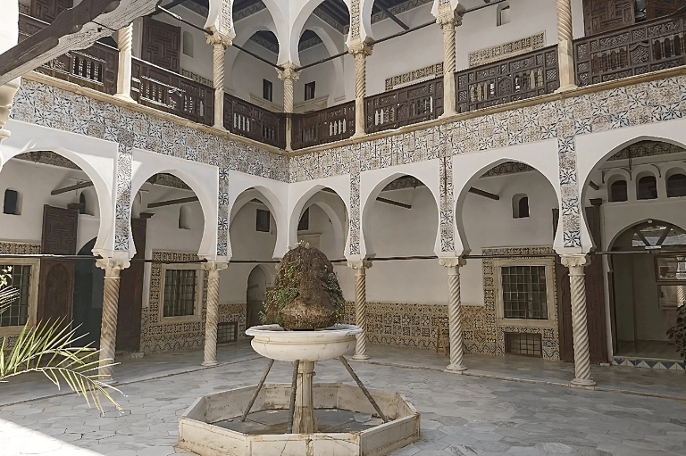 Historic Ottoman-style courtyard with ornate arches, intricate tilework, and central stone fountain, showcasing traditional architecture and design elements of casbah algiers