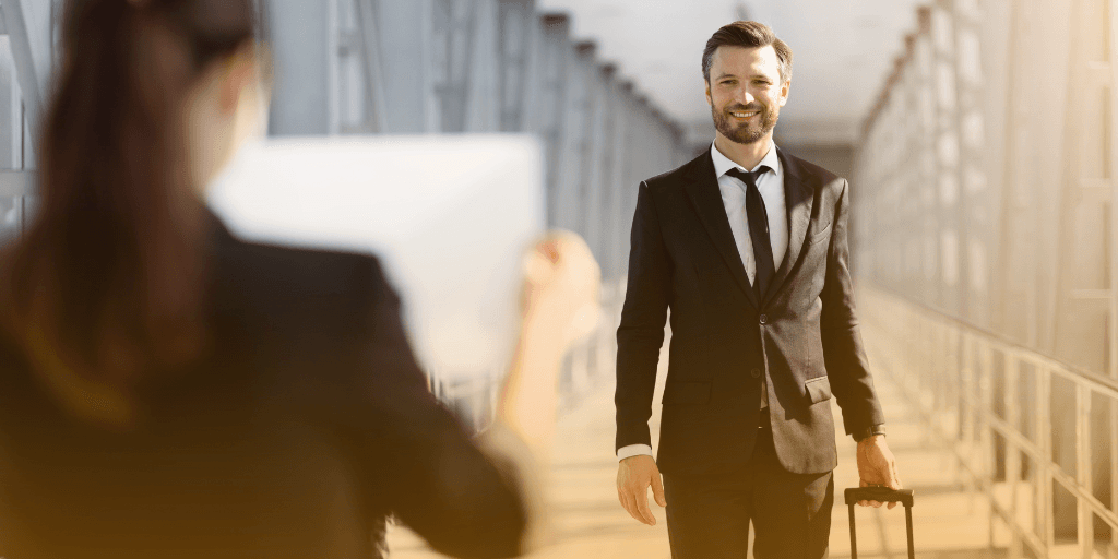 Algiers Airport vip Meet & Assist Services for a Smiling businessman in a suit walks through a bright airport walkway past a person holding a sign.