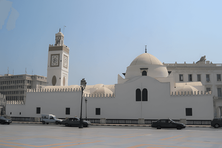 Algiers White mosque with a prominent clock tower stands beside a bright, clear plaza with traffic on a sunny day.