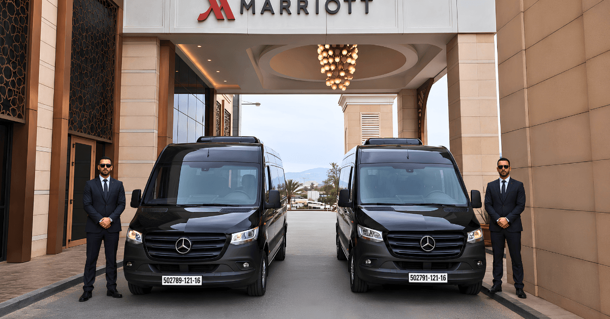 Deux hommes en costume se tiennent à côté de deux fourgonnettes Mercedes-Benz noires garées devant l'entrée de l'hôtel Marriott de Bab Ezzouar Alger.