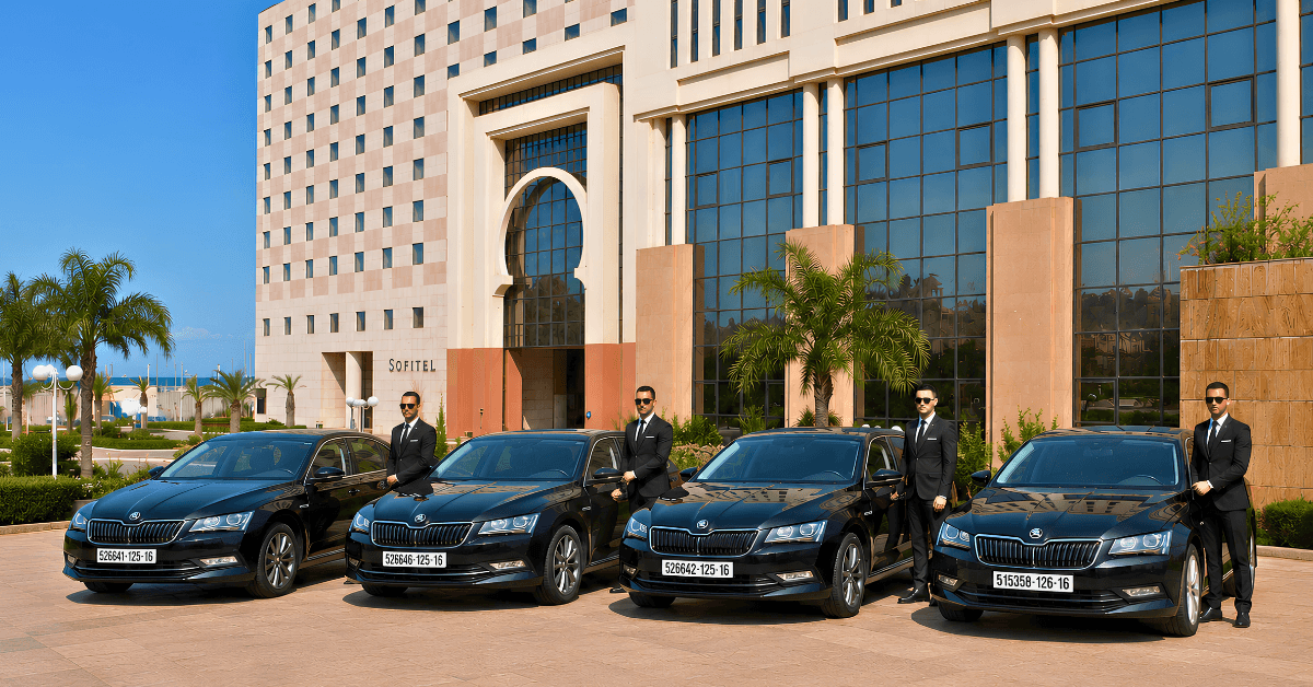 professional drivers in suits stand beside black Skoda superb sedans parked in front of a Sofitel Hamma gardens Algiers hotel.